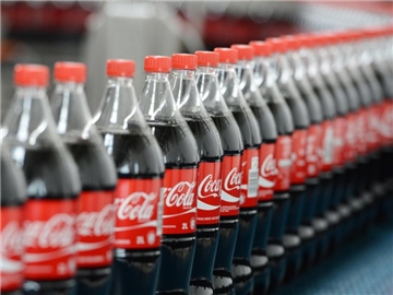 Flaschen mit Coca-Cola auf einem Transportband. Der Konzern will den Zuckeranteil seiner Produktpalette in Deutschland verringern. Foto: Jens Kalaene