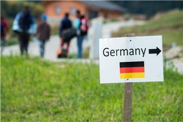 Flüchtlinge gehen nahe der deutschen Grenze hinter einem Schild mit der Aufschrift „Germany“. Foto: Armin Weigel/Illustration