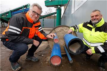 Flüssigboden-Experte Felix Föhre und GWA-Mitarbeiter Thomas Krajewski vor einem Versorgungsrohr, das zu Anschauungszwecken mit dem in Heeren-Werve entwickelten Flüssigboden verfüllt wurde. Der Boden, der sich um diese Leitungen schmiegt, muss nicht verdichtet werden – er verdichtet sich selbst. 