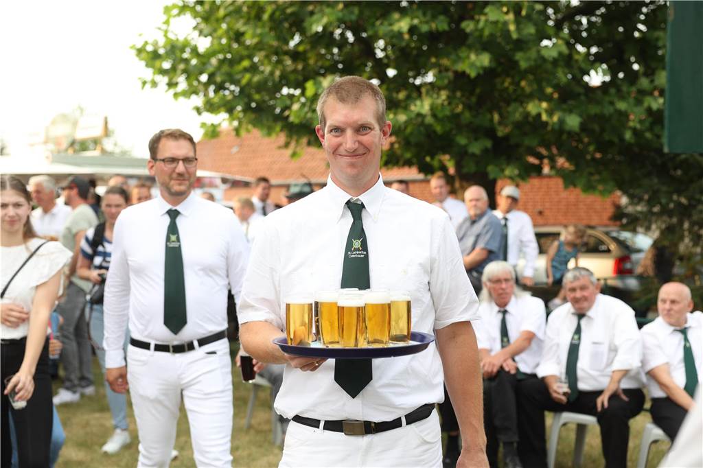 Ein junger Mann trägt ein Tablet mit mehreren Gläsern Bier. 