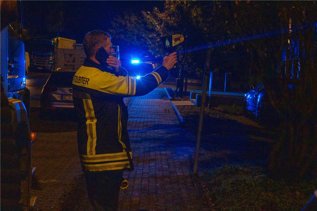 Seltsamer Gasaustritt sorgt für Nebel: Feuerwehr rückte nach Merklinde aus Ein Feuerwehrmann misst in der Dunkelheit mit einem Gerät an einem Einsatzort und telefoniert gleichzeitig. Auf seiner Jacke steht die Aufschrift Einsatzleiter.