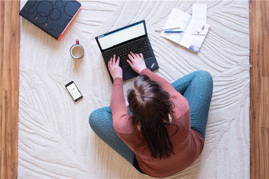 Homeoffice: Darf der Chef einfach mal vorbeischauen? Eine Frau sitzt im Homeoffice auf einem Teppich und arbeitet. Neben dem Laptop steht ein Kaffee.
