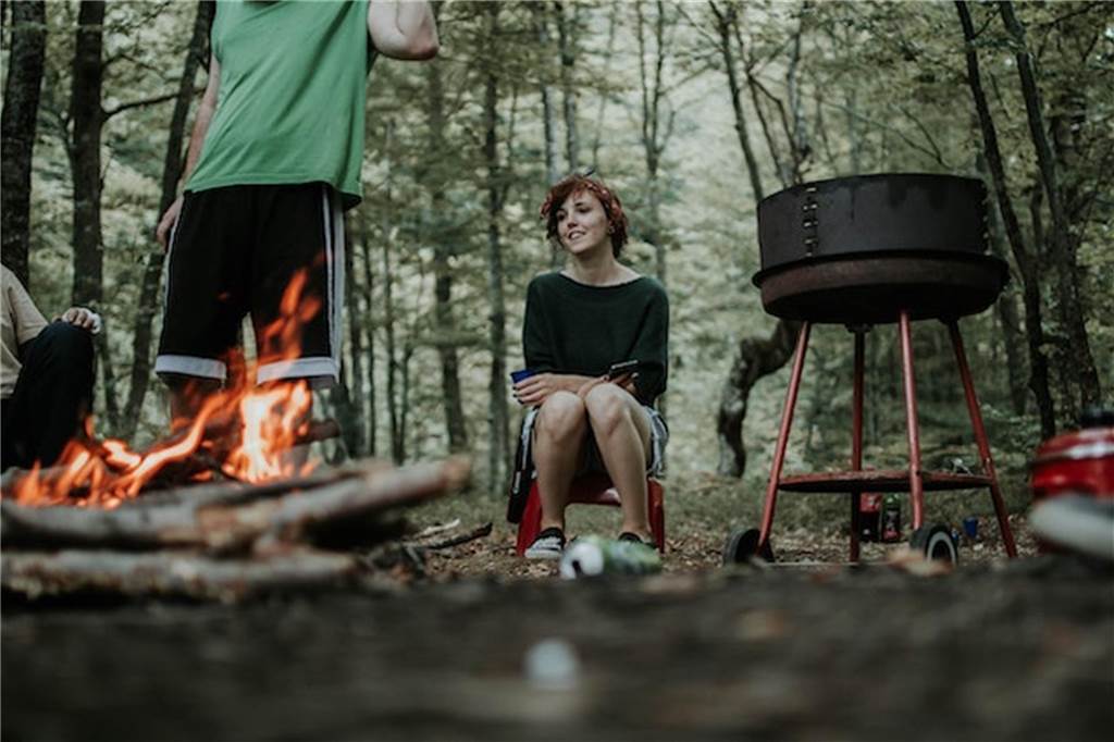 Freiheit und Freizeit genießen: Mit dem Camper durch NRW frau sitzt im wald an einem lagerfeuer