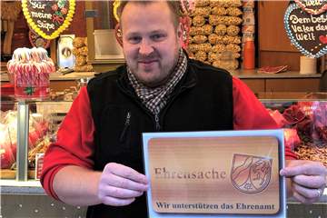 Händler André Brandt zeigt das Schild, das die Stände markiert, an denen Inhaber einer Ehrenamtskarte Vergünstigungen bekommen.