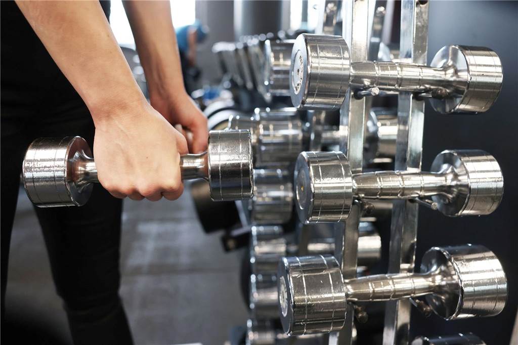 Jugendliche strömen in Fitnessstudios: Streben nach Muskeln kann krankhaft werden Eine Frau nimmt in einem Fitnessstudio zwei Hanteln von einem Ständer.