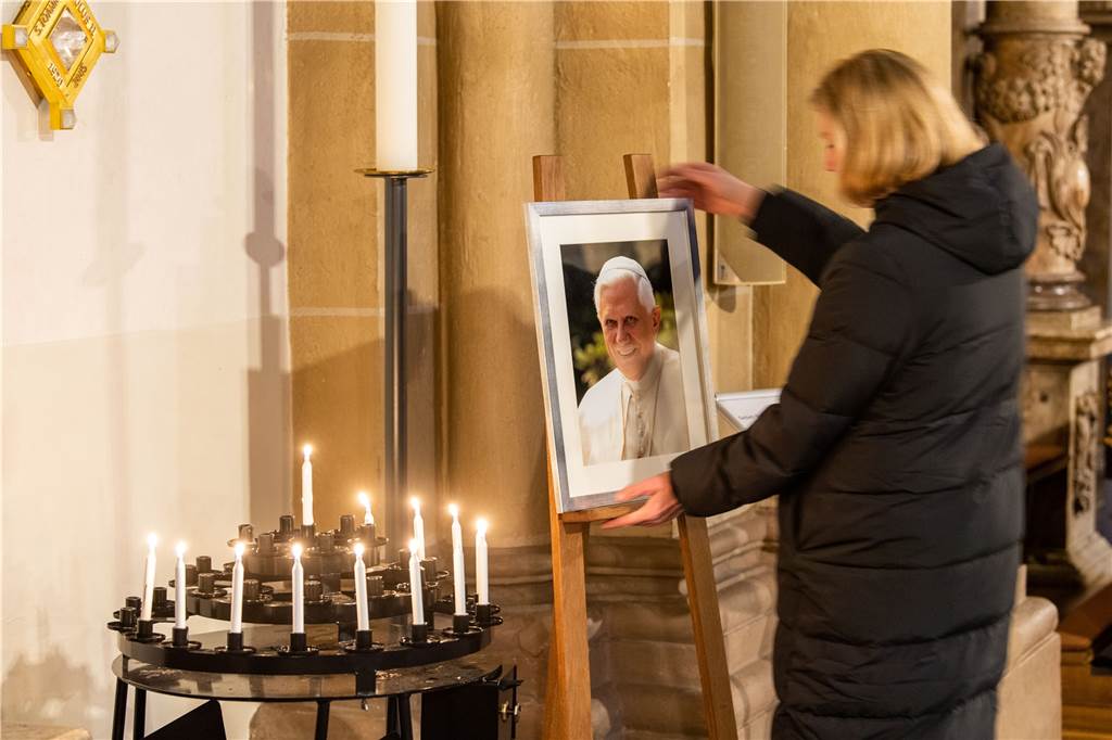 Heike Meyer, Leiterin der Kommunikation vom Erzbistum Paderborn, justiert ein Porträtbild vom emeritierten Papst Benedikt XVI. hinter Andachtskerzen Paderborner Dom. 