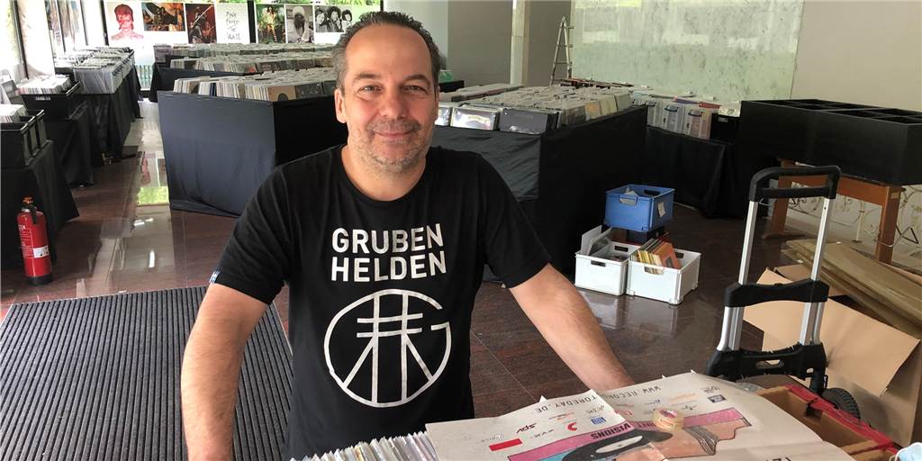Heinz-Bernd Töns steht im Plattenbau in Schermbeck hinter einem Tisch mit vielen Schallplatten.