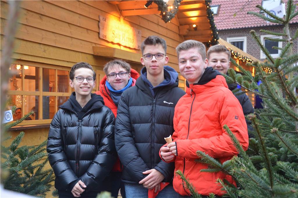 Eine Gruppe Jugendlicher steht vor einer Holzhütte umgeben von Tannenbäumen. 