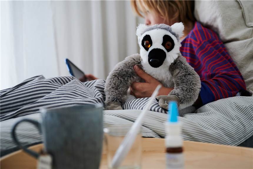 Rätselhafte Hepatitis-Fälle bei Kindern: Erster Fall in Deutschland bekannt Ein Fieberthermometer, Nasenspray und eine Tasse Tee stehen vor einem Bett, in dem ein Kind mit Kuscheltier sitzt und auf ein Tablet schaut.