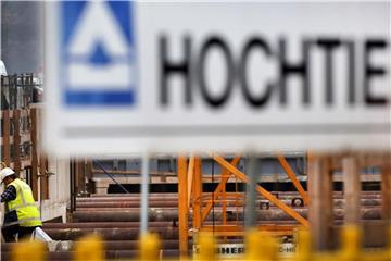 Hinter einem Logo des Baukonzerns Hochtief steigt ein Arbeiter in eine Baustelle. Foto: Martin Gerten/Archiv