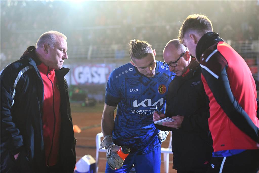 So geht Pokalsieg: Im Dunkeln des Stimberg-Stadions zündet „Ö“ erst mal eine „Fluppe“ an Spvgg. Erkenschwicks Torhüter Rafael Hester bekommt im Westfalenpokalspiel gegen Preußen Münster am 28. September 2022 von Torwarttrainer Christian Kelm letzte Tipps vor dem Elfmeterschießen. Links Co-Trainer Jörg Weißfloh, rechts Ersatzkeeper Philipp Amft.