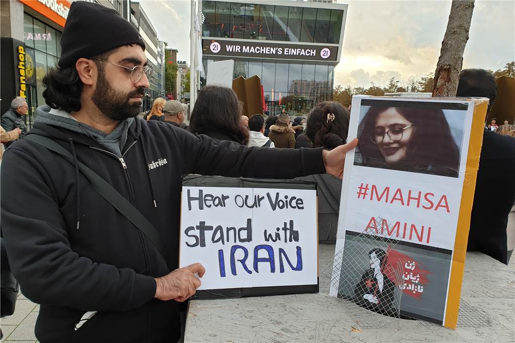 Demo für Mahsa Amini: Demonstranten schneiden sich aus Protest die Haare ab „Hört unsere Stimme, steht mit dem Iran“, ist auf dem Plakat eines Demonstranten zu lesen.