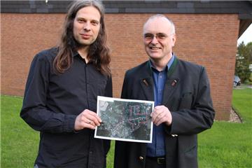 Holger Langer (l.) und Pater Altfried Kutsch zeigen vor dem evangelischen Gemeindehaus, dem Ort für den Abschlussgottesdienst, eine Übersicht des neuen Prozessionsweges.