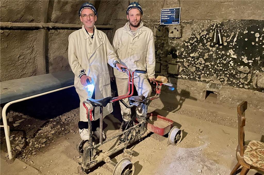Dritter Escape-Room geplant: Im Trainingsbergwerk knifflige Rätsel lösen Dennis Hölker und Standortleiter stehen im Trainingsbergwerk Recklinghausen in einem unverputzten, sandigen Escape-Room an einem alten Grubenrad.