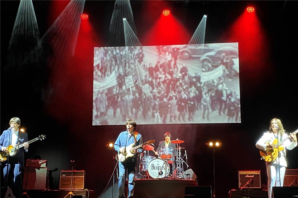 Beatles-Musical: „Kann froh sein, dass er nicht mit Ruhrpott-Slang singen muss“ Im Hintergrund liefen auf einer Leinwand schwarz-weiße Videoausschnitte von damaligen Bandauftritten der Beatles.
