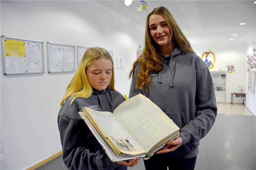 Zwei Schülerinnen halten die Schulchronik in den Händen. 