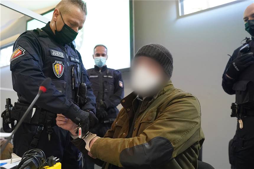 Ehefrau und zwei Männer erschossen: Zahnarzt nach Dreifachmord verurteilt Ein Justizbeamter entfernt die Handschellen des Angeklagten (2.v.r) im Sitzungssaal der Außenstelle des Landgerichts zu Beginn des Prozesstages wegen eines Dreifachmordes.
