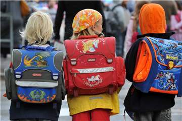 Drei Kinder laufen mit ihren Schulranzen zur Schule.