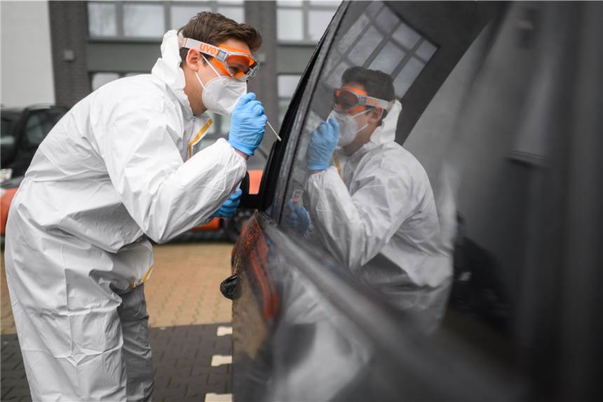 Amtsärzte kritisieren „lockereren Umgang mit Corona“: Aktuelle Zahlen stimmen nicht Ein Mitarbeiter entnimmt einen Abstrich von einem in einem Auto sitzenden Patienten für einen PCR-Test auf das Coronavirus vor einer Arztpraxis.