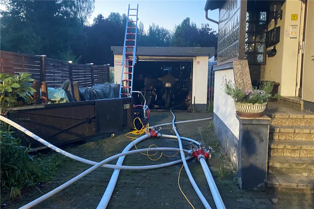 Garagenbrand in Groppenbruch greift auf Gartenhaus über Löschrohre der Feuerwehr in der Einfahrt vor der ausgebrannten Garage.