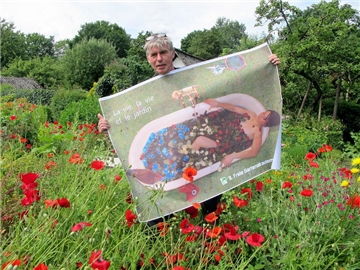 In Blumen baden: Wilm Weppelmann steht mit dem Plakat zur 9. Gartenakademie in seinem Schrebergarten.