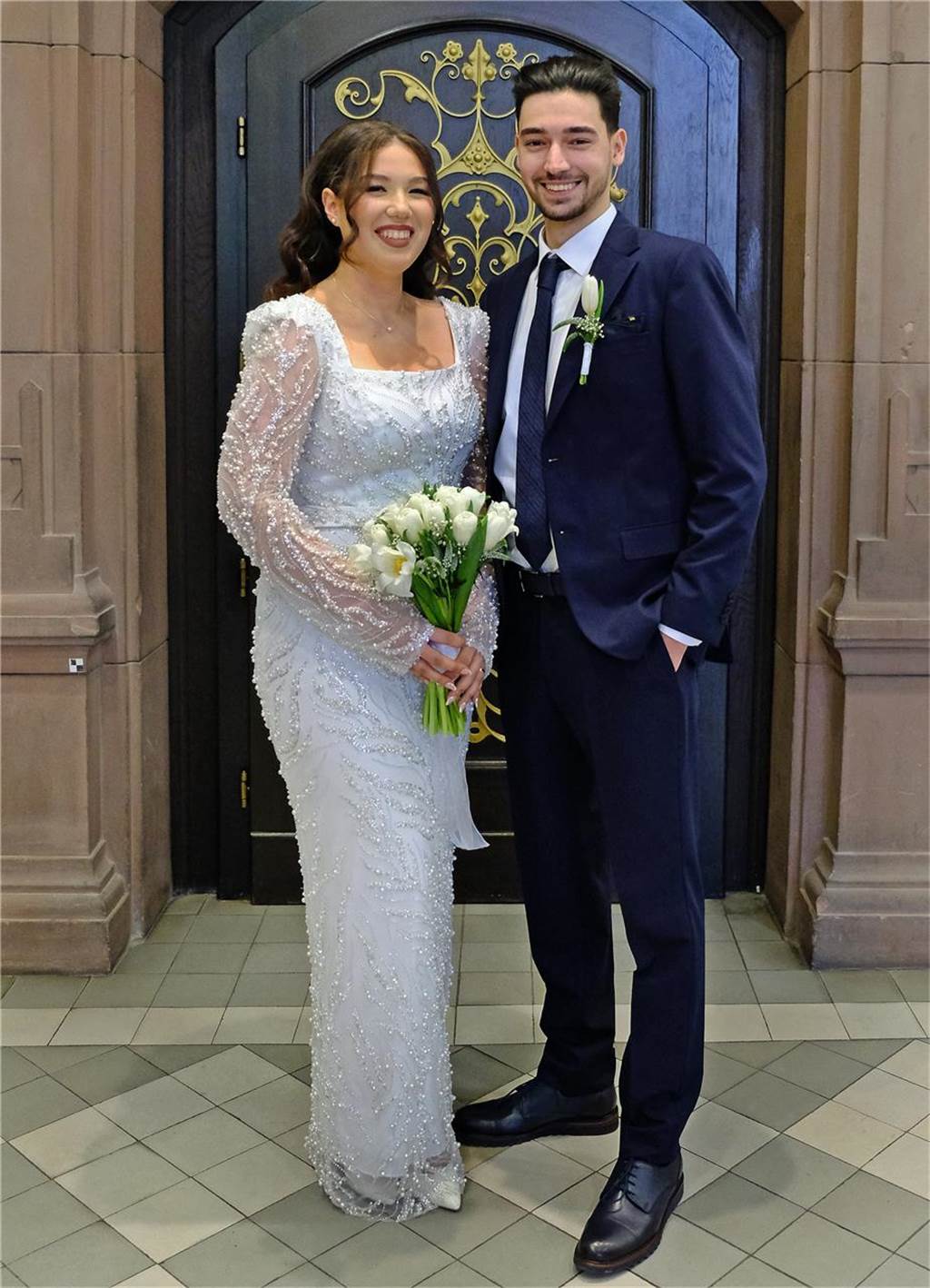Das frisch vermählte Ehepaar Ceyda Gümüs und Kaan Coskun steht in Brautkleid und Anzug vor dem Rathaus Recklinghausen.