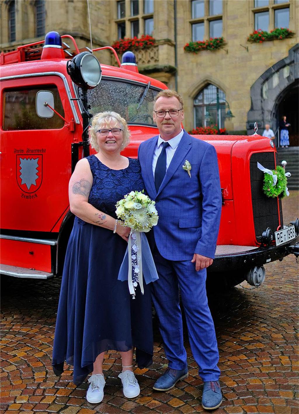 Brautpaar Reinhild Vadder und Uwe Starke stehen nach ihrer Trauung vor dem Rathaus in Recklinghausen, im Hintergrund steht ein historisches Löschfahrzeug der Feuerwehr, das mit Brautschmuck verziert ist