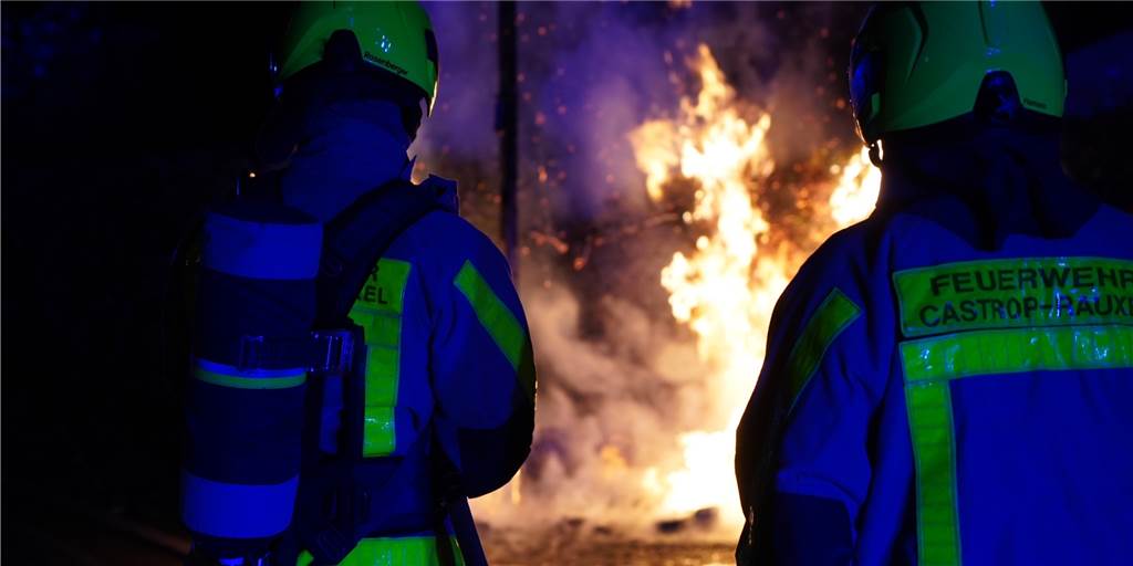 Wieder brennen Mülltonnen in Castrop-Rauxel: Wer war es diesmal? Zwei Einsatzkräfte der Feuerwehr Castrop-Rauxel stehen vor einer brennenden Mülltonne.