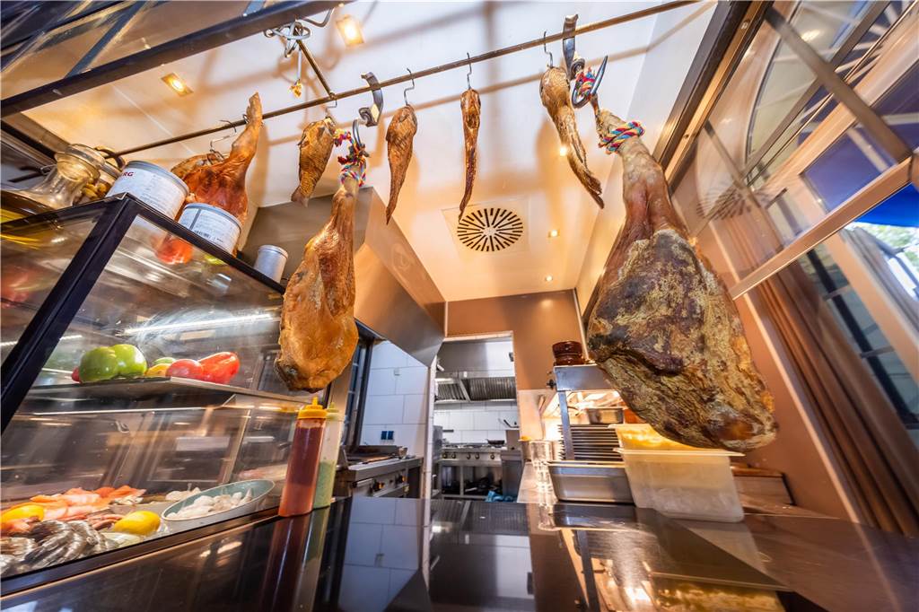 Auf der Jagd nach kleinen Köstlichkeiten – Tapasbar „Chuzo“ im Check In der offenen Küche des "Chuzo" hängen geräucherter Fisch und Schinken.
