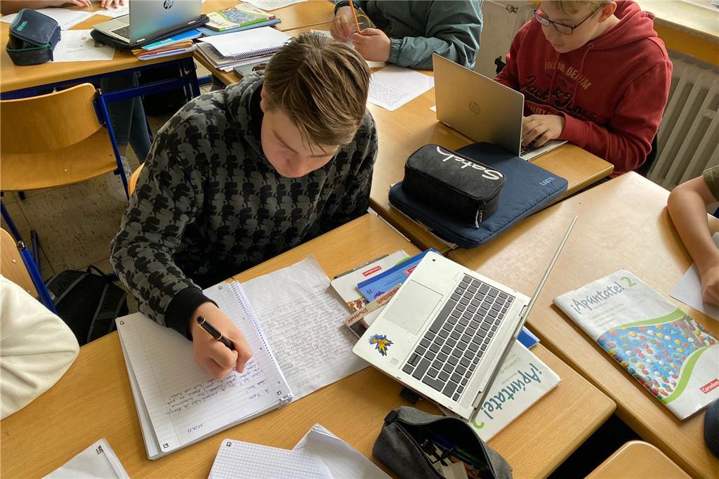 Junge sitzt am Tisch in der Schule und schreibt einen Brief auf einen Block. 
