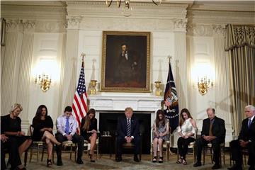 In einem großen Kreis sitzen Überlebende und Angehörige im Weißen Haus um den US-Präsidenten, auch die früherer Massaker an US-Schulen. Foto: Carolyn Kaster/AP