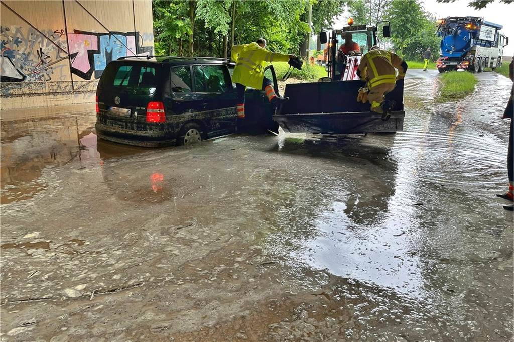 Auto steht in einer vollgelaufenen Unterführung. Feuerwehrmänner stehen drumherum.