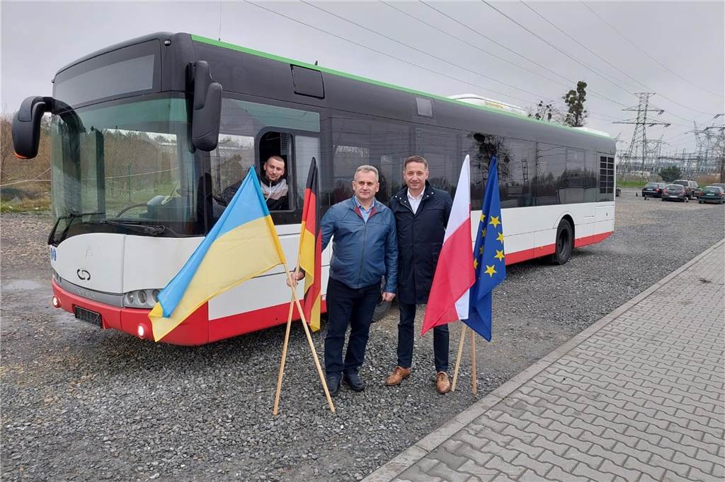 Schulbus für ukrainische Stadt Bar dank vieler Spenden Männer stehen vor einem Bus und halten Fahnen.