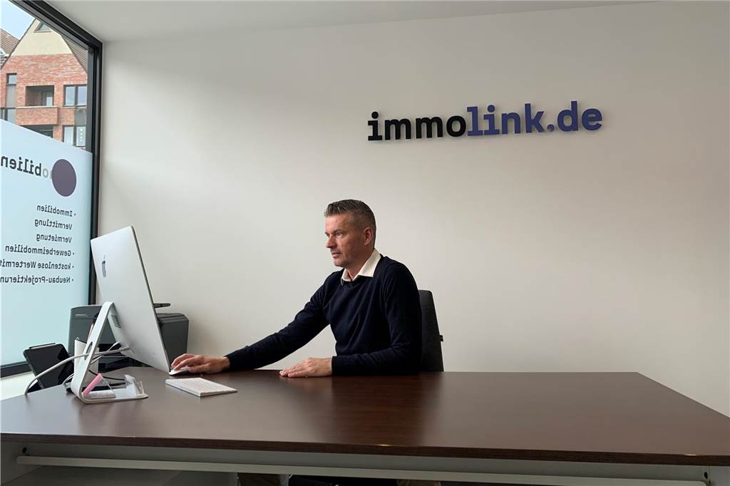 Makler Anel Kicin beantwortet die drängendsten Fragen zum Immo-Kauf Der Makler Anel Kicin sitzt am Schreibtisch in seinem Büro. Im Hintergrund ist eine Schriftzug mit dem Namen seines Unternehmens "immolink.de " zu sehen.