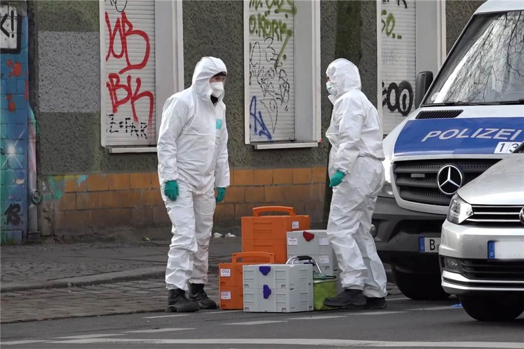 RAF-Fahndung in Berlin: Polizei stürmt weitere Wohnung in Friedrichshain Einsatzkräfte der Spurensicherung stehen in weißen Anzügen gekleidet an einem Grundstück.