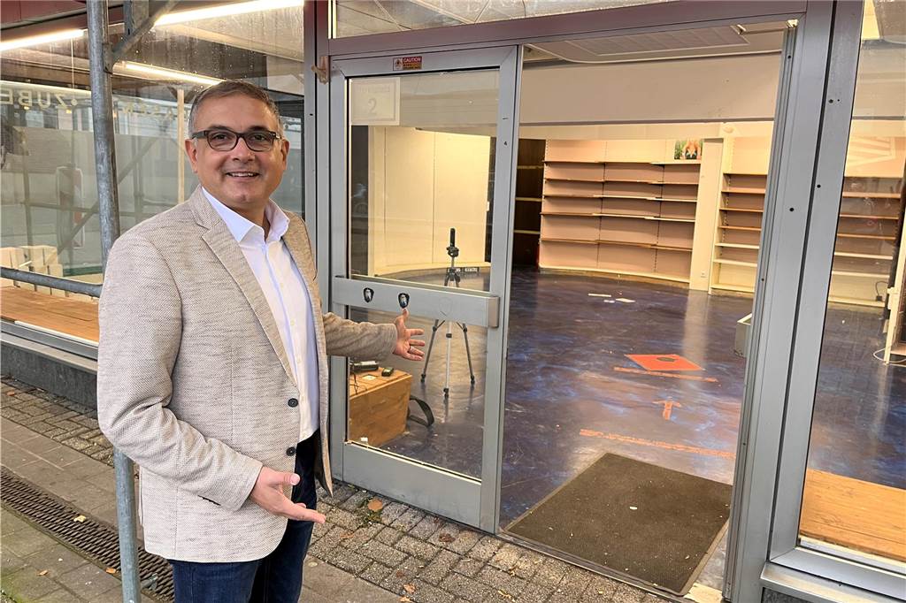 Iraklis Paschalidis vor einer geöffneten Ladenlokaltür mit einladender Geste.
