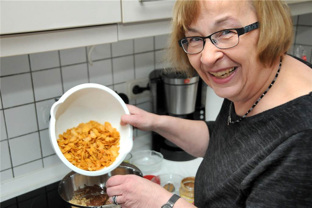 Cornflakes baden für das Zuckerguss-Magazin in Schokolade Irmhild Brauckmann kippt die abgewogenen Cornflakes in den Topf mit der flüssigen Schokoladenmasse.