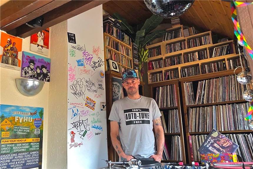 Der Lockdown hat den Musiker und DJ „Der Wolf“ erfinderisch gemacht Jens Albert hat kurzerhand sein Wohnzimmer als TV-Studio umfunktioniert und legt dort mit Gästen zusammen auf, die sich an der weißen Wand verewigen. Das T-Shirt zeigt seine Labelmarke.