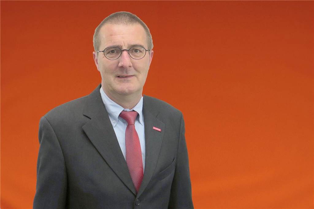 Ein Mann mit Brille und roter Krawatte steht vor einem orangen Hintergrund. (Archivbild)