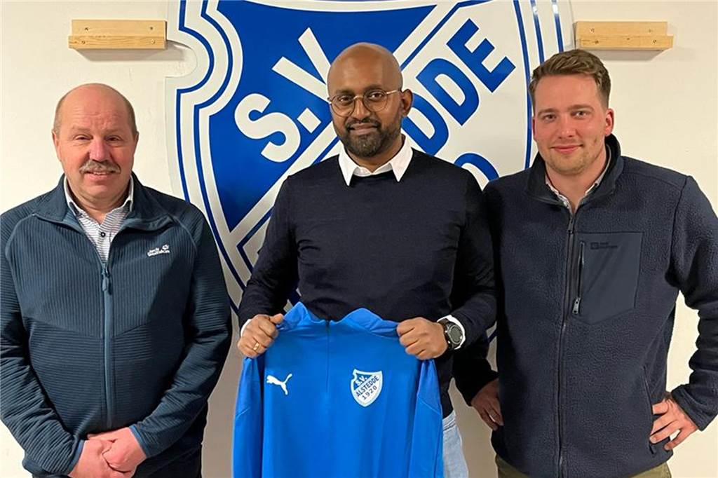 BW Alstedde hat einen neuen Trainer gefunden Joachim Knappmann und Benedikt Kuhne stehen mit Athavan Varathan, dem neuen Trainer von Blau-Weiß Alstedde, vor einem Alstedde-Logo an der Wand.