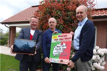 Drei Männer halten ein Plakat für eine Wahl-Veranstaltung.