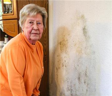 Karin Backe in ihrem Wohnzimmer, wo die Feuchtigkeit trotz einer neuer Tapete wieder durchgekommen ist und Schimmelpilz entstanden ist.