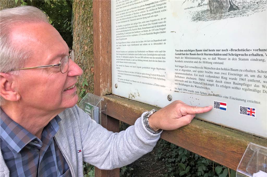 Erler Femeiche kann jetzt auch englisch und niederländisch Karl-Josef Behler zeigt auf die neuen QR-Codes auf der Tafel der Femeiche, die per Internet die Übersetzung der Tafeln ins Niederländische und Englische aufs Smartphone bringen.