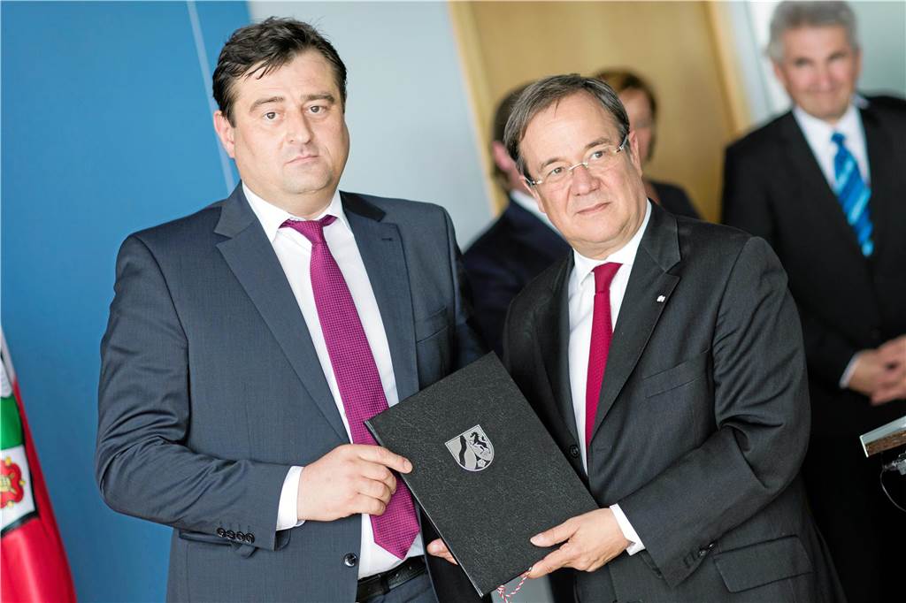 Mathias Richter und Armin Laschet stehen nebeneinander. Sie halten eine dunkle Mappe mit NRW-Wappen in den Händen.