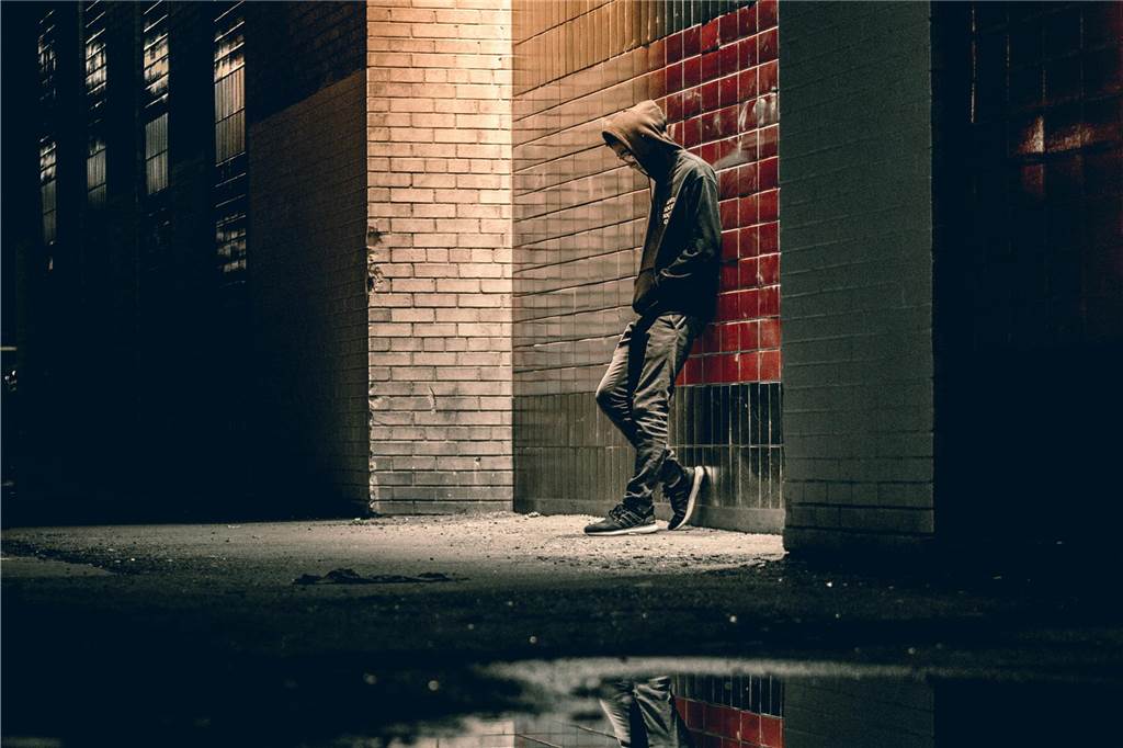 Klaas (35) ist kokainabhängig: „Meine Sucht ist ein Beziehungskiller“ Ein junger Mann steht nachts mit der Kapuze ins Gesicht gezogen an einer Wand gelehnt.