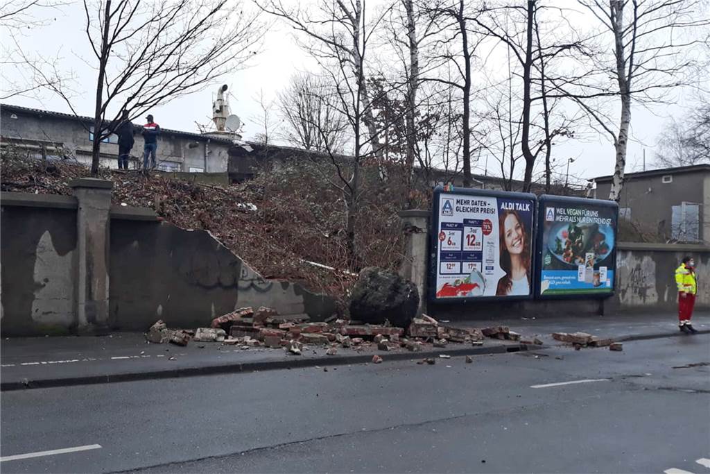 Riesiger Findling durchschlägt Mauer – Trümmerteile verletzen Kind Kurz nach dem Unglück. Während Sanitäter das verletzte Kind versorgen, schauen die mutmaßlichen Verursacher auf die Unfallstelle.