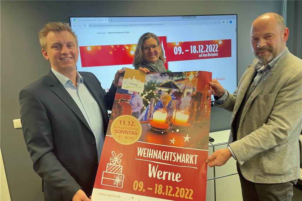Lars Werkmeister (v. l.) und Britta Löchter vom Werne Marketing präsentieren gemeinsam mit Händler Hubertus Waterhues das Plakat für den Weihnachtsmarkt Werne 2022.