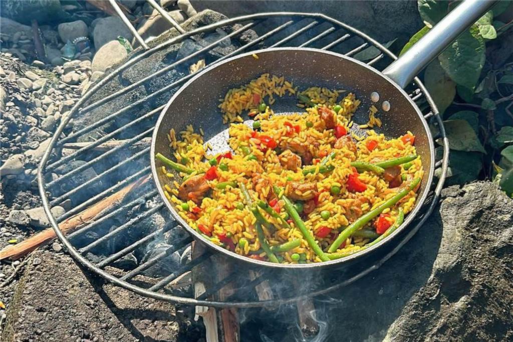 Die Waltons lassen grüßen: Wenn die Jungs Übernachtungsgäste haben Über einem Lagerfeuer liegt ein Rost mit einer Pfanne darauf. In der Pfanne ist Paella.