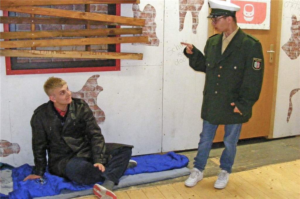Zwei Nachwuchsschauspieler feiern ihre Bühnenpremiere „up Platt“ Lukas Nolte sitzt als Landstreicher am Boden, Jonas Florien steht als Polizist daneben