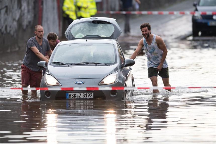Gewitterfront trifft NRW - Wind und starker Regen Männer schieben am 19.07.2017 ein Auto aus dem Wasser einer überfluteten Straße in Köln (Nordrhein-Westfalen). In Köln hatte es zuvor ein starkes Gewitter gegeben.
